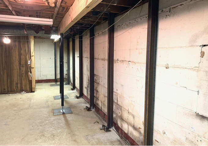 I-beam bowed basement wall repair: steel I-beams installed along a cracked basement wall, from floor plates to the joists