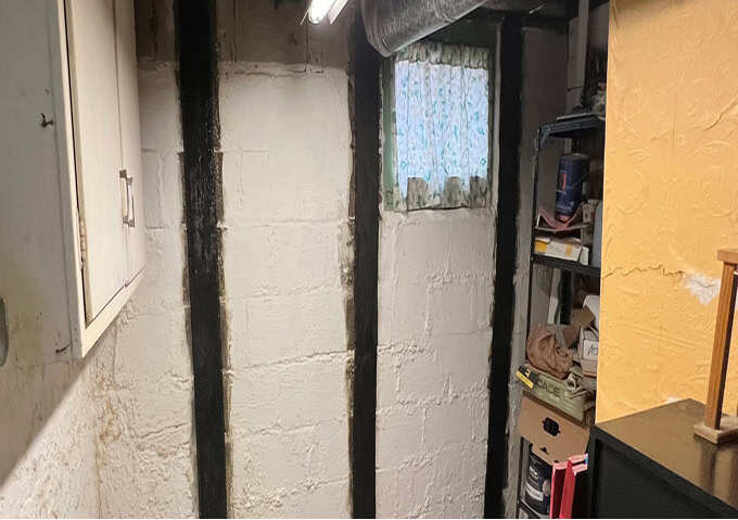 Carbon fiber wall straps bonded vertically to a painted basement block wall beside a window