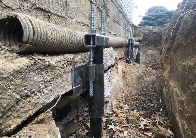 Helical pier foundation repair: a steel pier and bracket supporting the footing of a foundation wall in an excavated trench